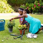 Two african american sisters planting together at backyard garden