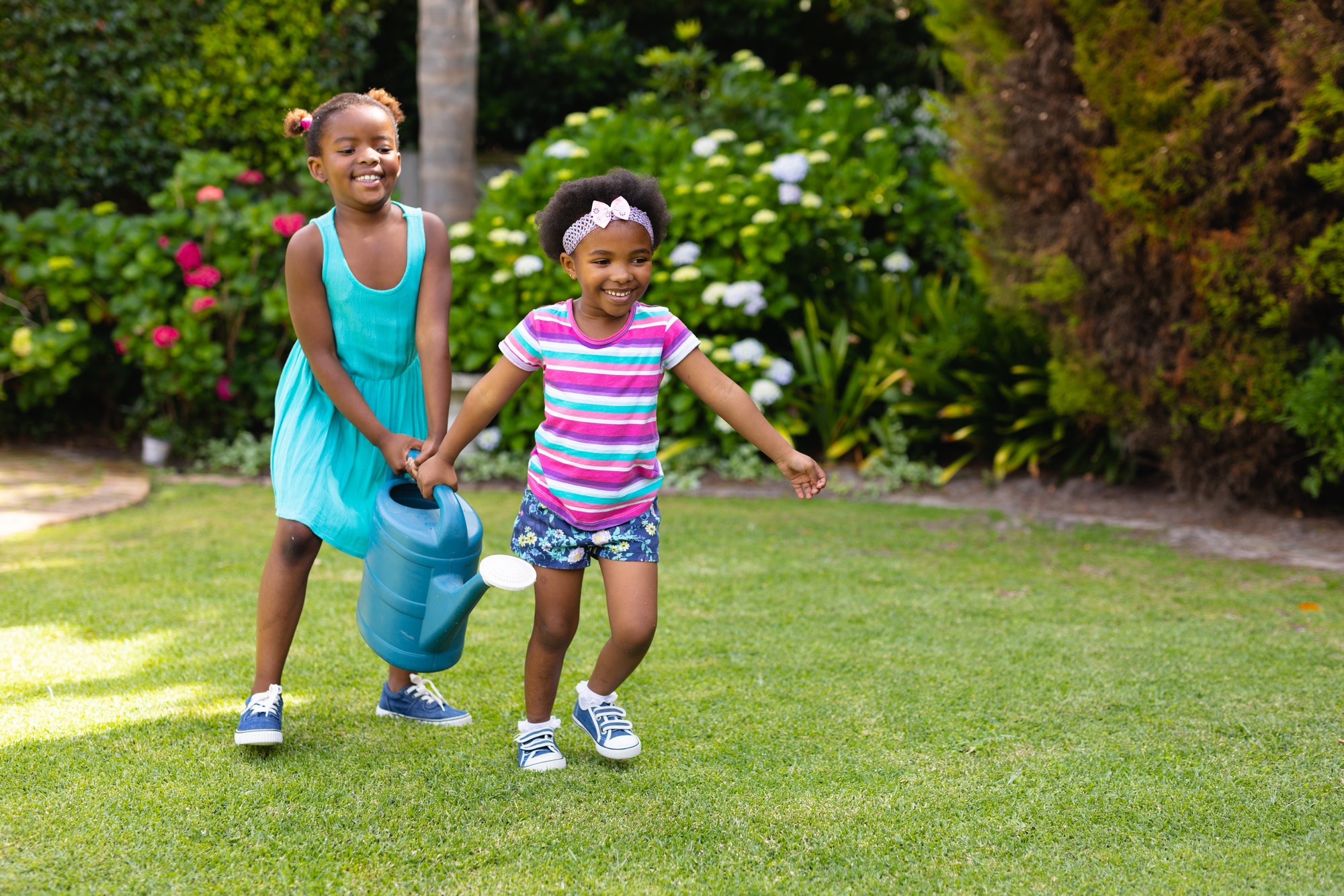 Two african american sisters with watering can running in garden